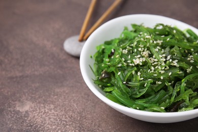 Photo of Tasty seaweed salad in bowl served on brown table, closeup. Space for text
