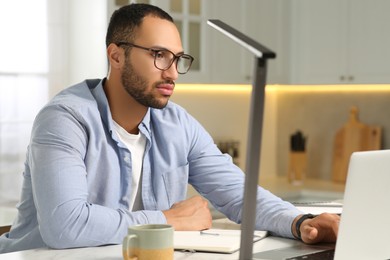 Photo of Young man working on laptop at desk in kitchen. Home office