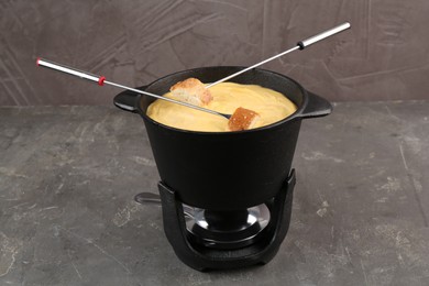 Fondue pot with tasty melted cheese, forks and bread on grey table