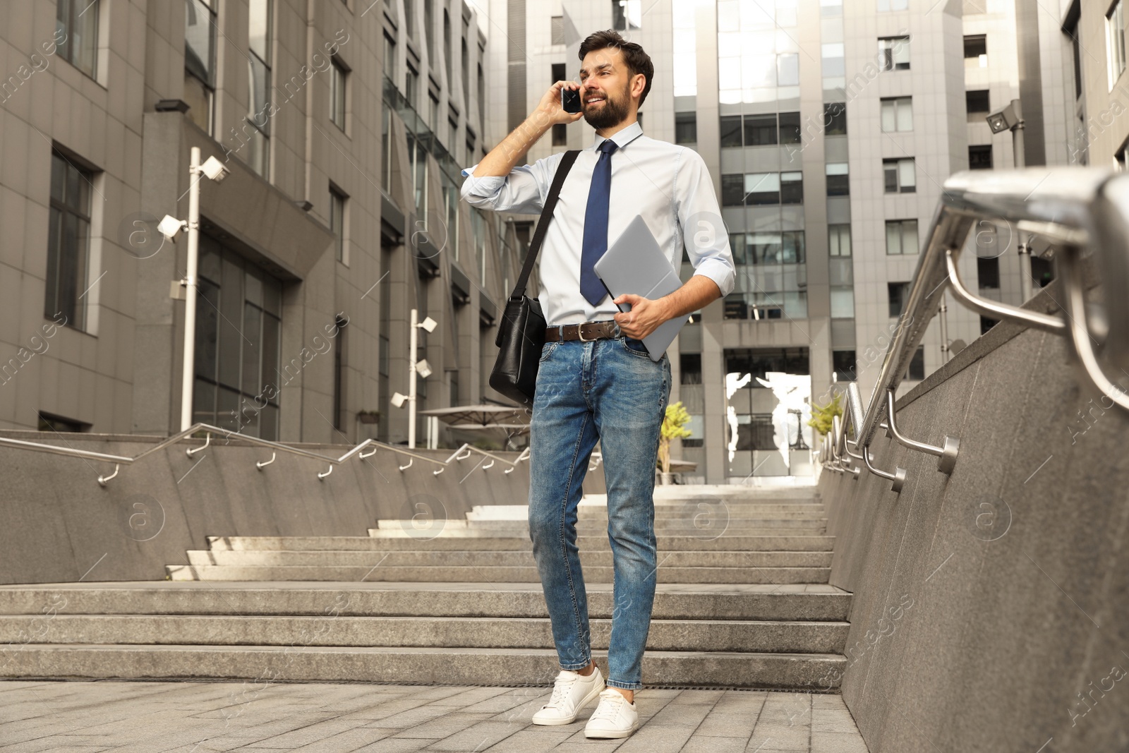 Photo of Handsome man with laptop talking on phone in city