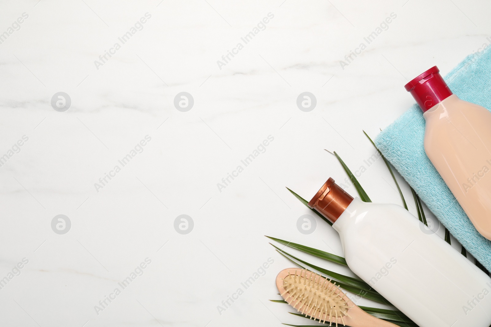 Photo of Shampoo bottles, hair brush, towel and palm leaf on white marble table, flat lay. Space for text