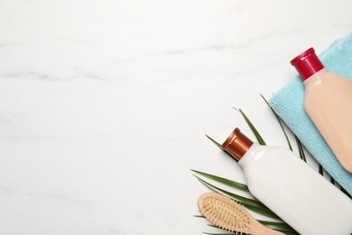 Photo of Shampoo bottles, hair brush, towel and palm leaf on white marble table, flat lay. Space for text