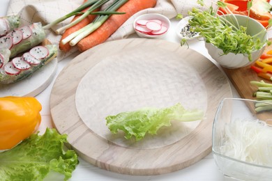 Photo of Rice paper and other ingredients for spring rolls on white wooden table