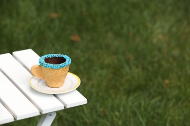 Delicious edible biscuit coffee cup decorated with sprinkles on white wooden table outdoors, space for text