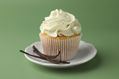 Photo of Tasty cupcake with cream and vanilla pods on green background