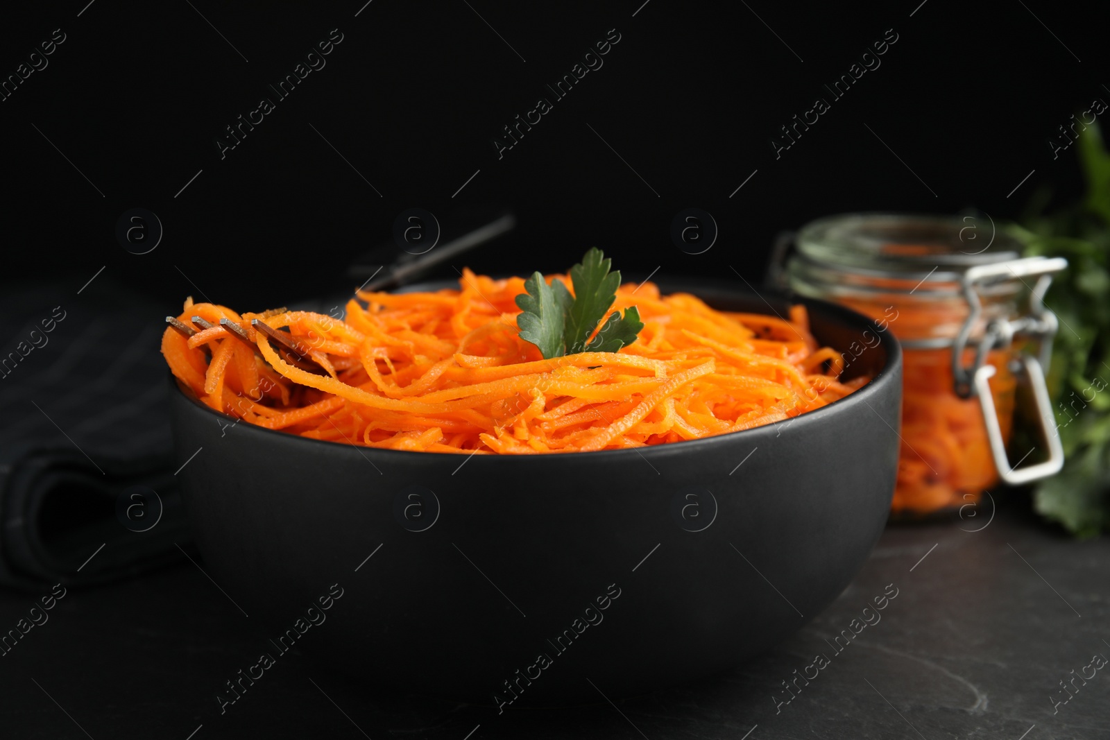 Photo of Delicious Korean carrot salad with parsley in bowl on black table