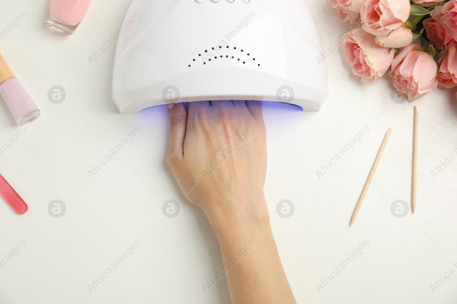 Photo of Woman using ultraviolet lamp to dry gel nail polish at white table, top view