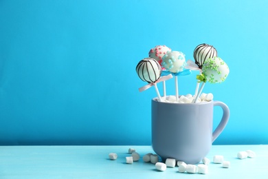 Photo of Tasty cake pops in cup with marshmallow on wooden table against light blue background. Space for text