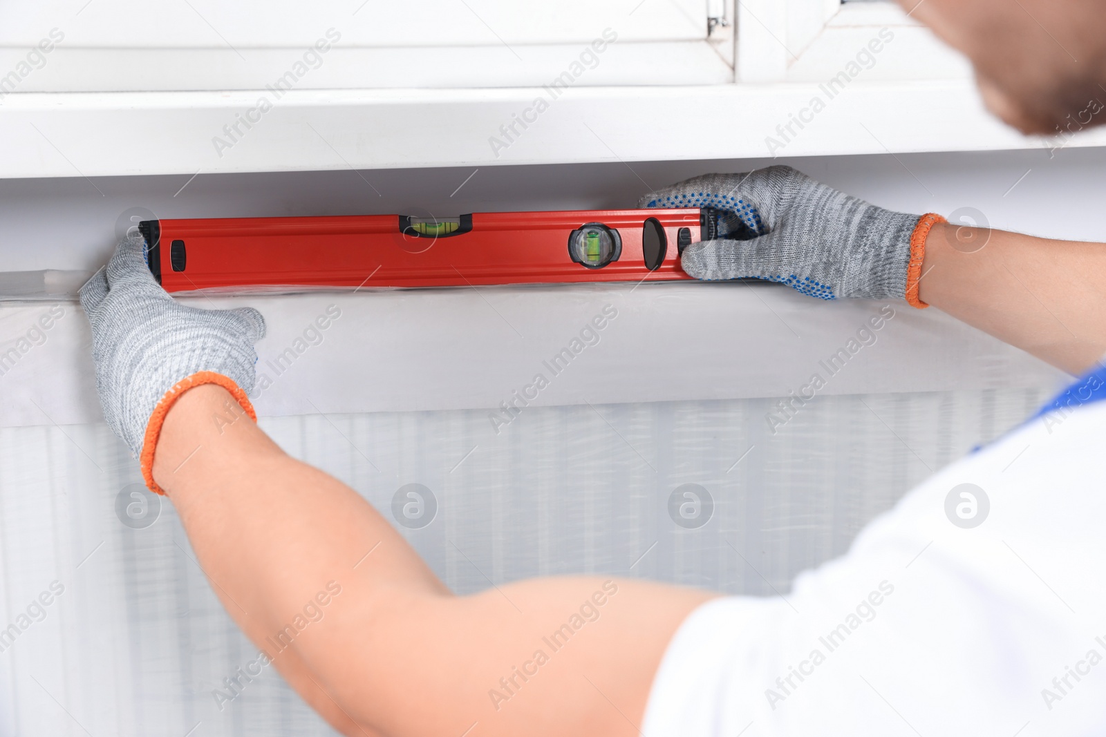Photo of Professional plumber using bubble level for installing new heating radiator indoors, closeup