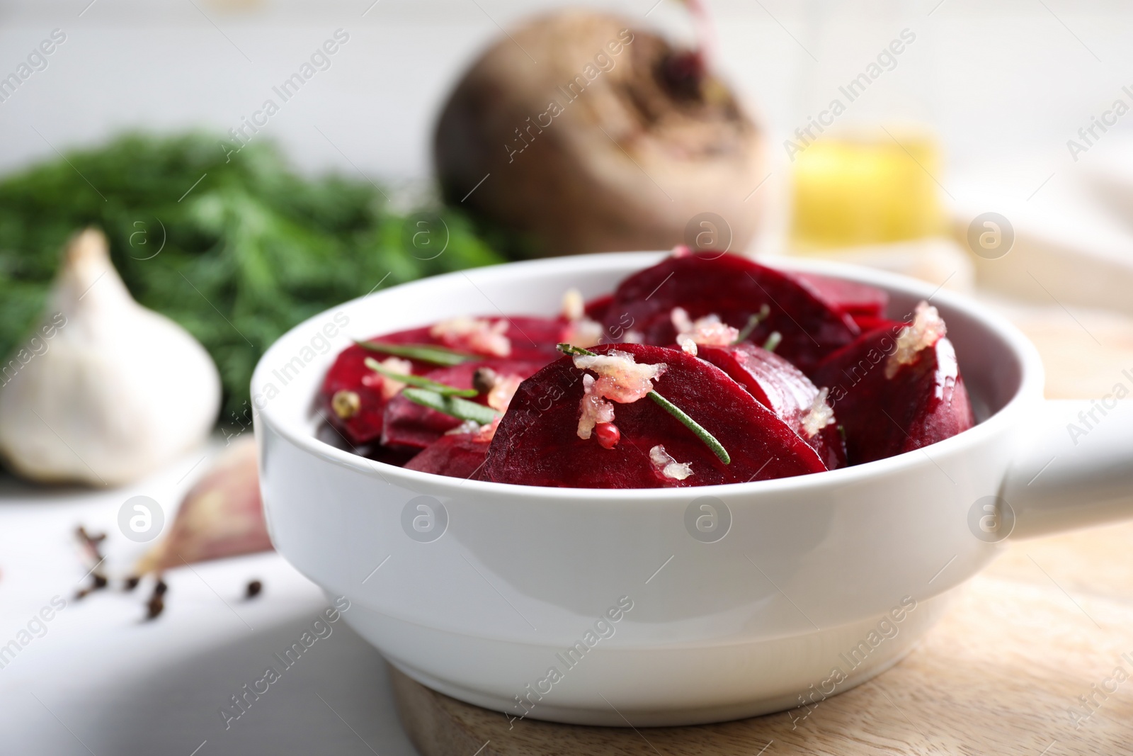 Photo of Raw beetroot slices, garlic and rosemary in bowl on white table, closeup