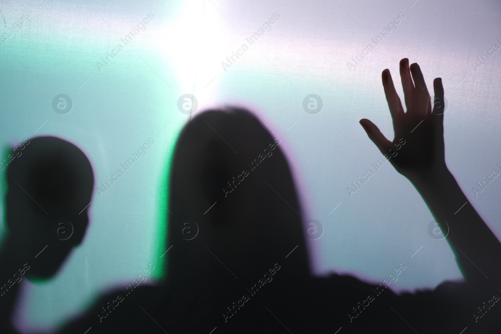 Photo of Silhouette of creepy ghost with skull behind cloth against color background