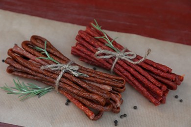Photo of Tasty dry cured sausages (kabanosy) and spices on parchment paper