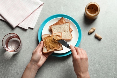 Woman spreading peanut butter on toast bread at table, top view