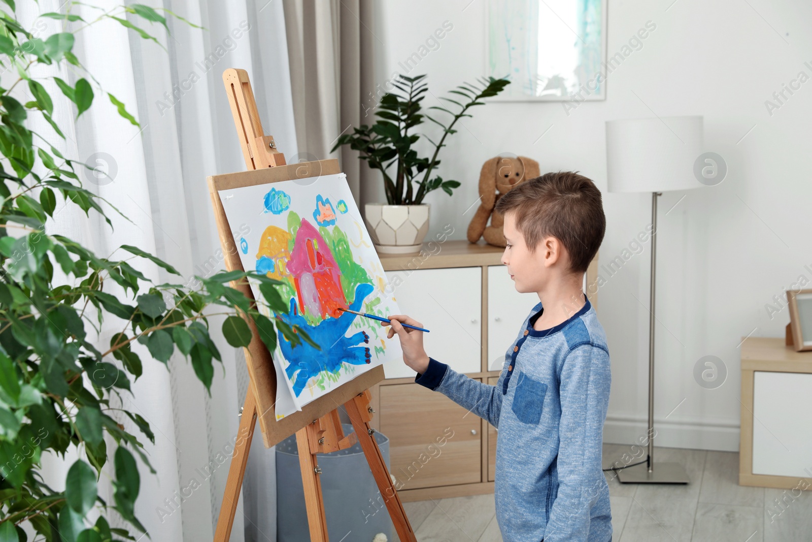 Photo of Little child painting picture using easel at home