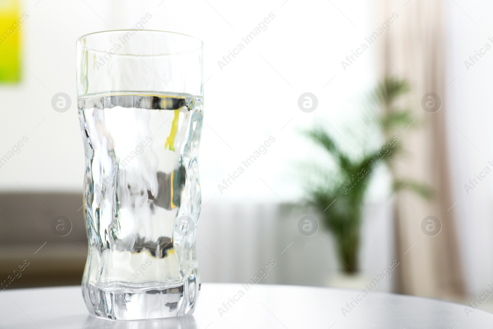 Photo of Glass of water on table in room, space for text. Refreshing drink