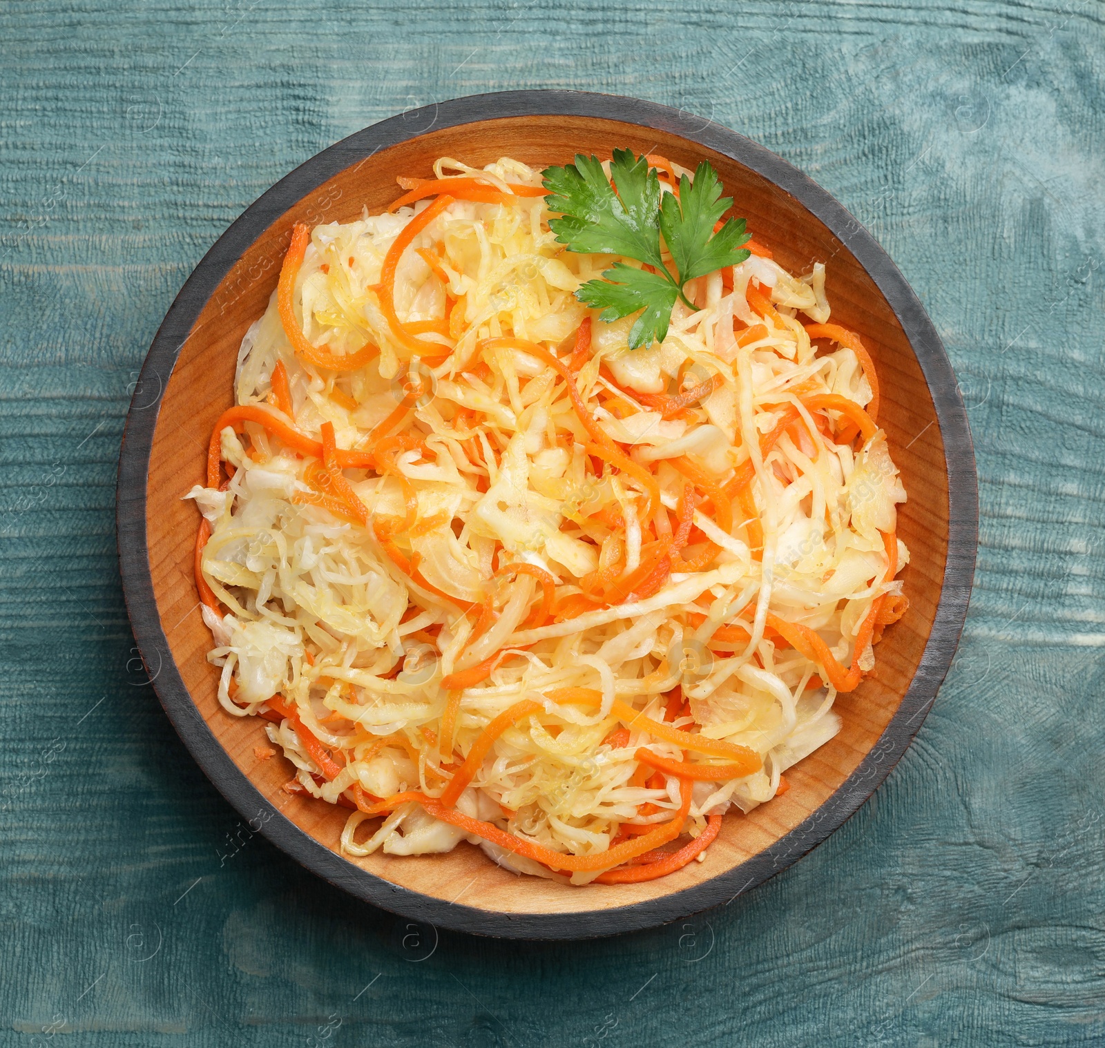 Photo of Tasty fermented cabbage with carrot on blue wooden table, top view