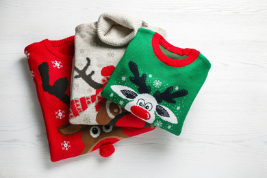 Folded warm Christmas sweaters on white wooden table, top view