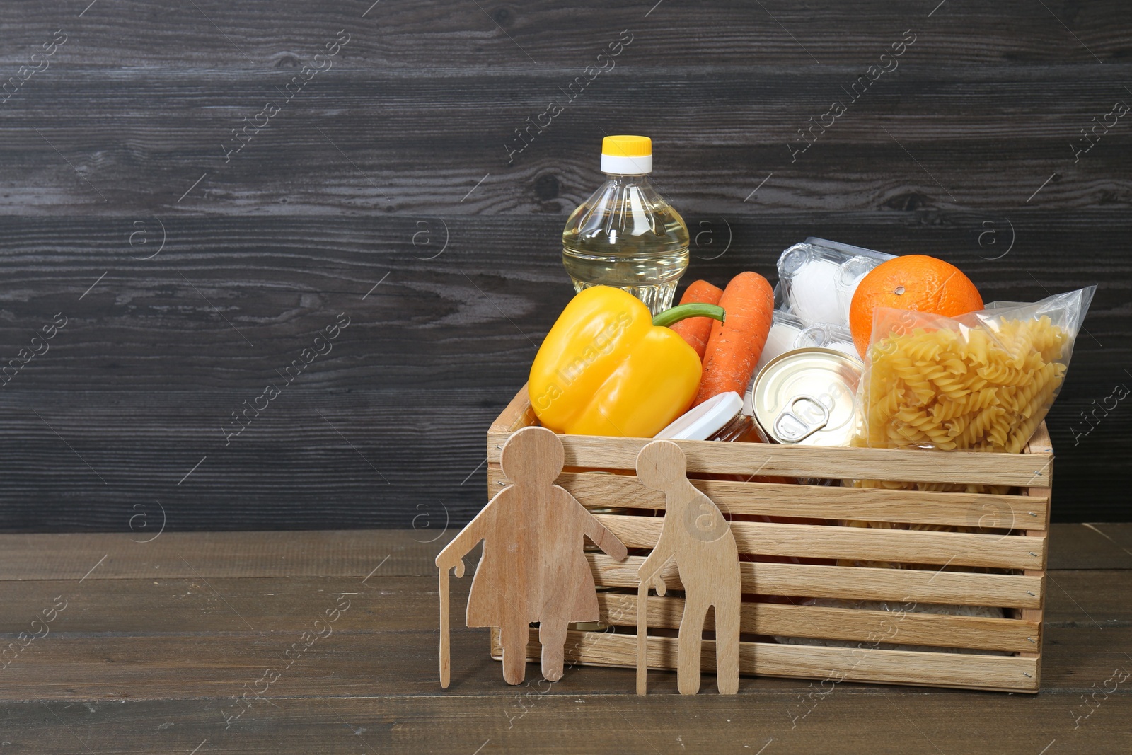 Photo of Humanitarian aid for elderly people. Crate with donation food and figures of couple on wooden table. Space for text