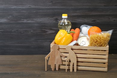 Photo of Humanitarian aid for elderly people. Crate with donation food and figures of couple on wooden table. Space for text
