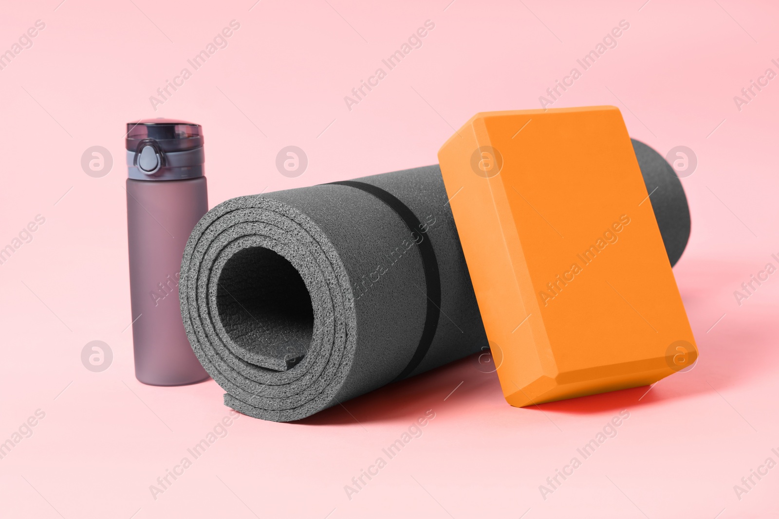 Photo of Grey exercise mat, yoga block and bottle of water on pink background