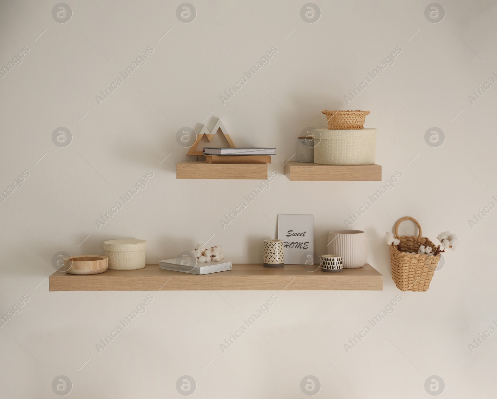 Photo of Wooden shelves with books and different decorative elements on light wall