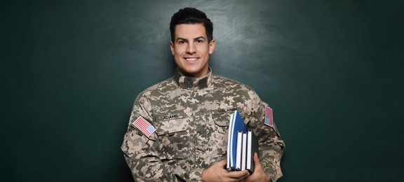 Military education. Cadet with notebooks near green chalkboard