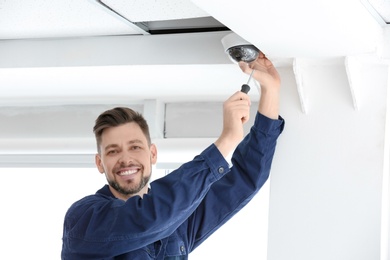 Technician installing CCTV camera on ceiling indoors