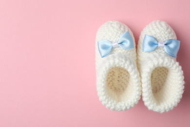 Handmade child's booties on pink background, flat lay with space for text