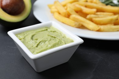 Plate with french fries, guacamole dip and avocado served on black table, closeup