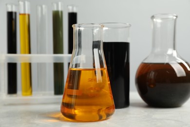 Photo of Laboratory glassware with different types of oil on white table, closeup