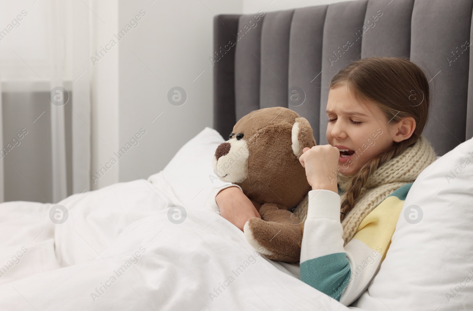 Photo of Sick girl with teddy bear coughing on bed at home