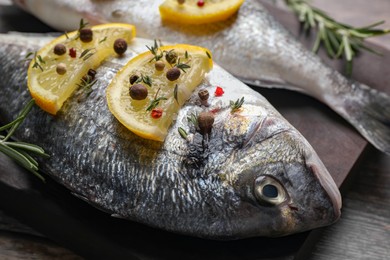 Fresh dorado fish, lemon slices and peppercorns on dark board, closeup