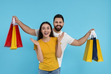 Photo of Excited couple with shopping bags on light blue background