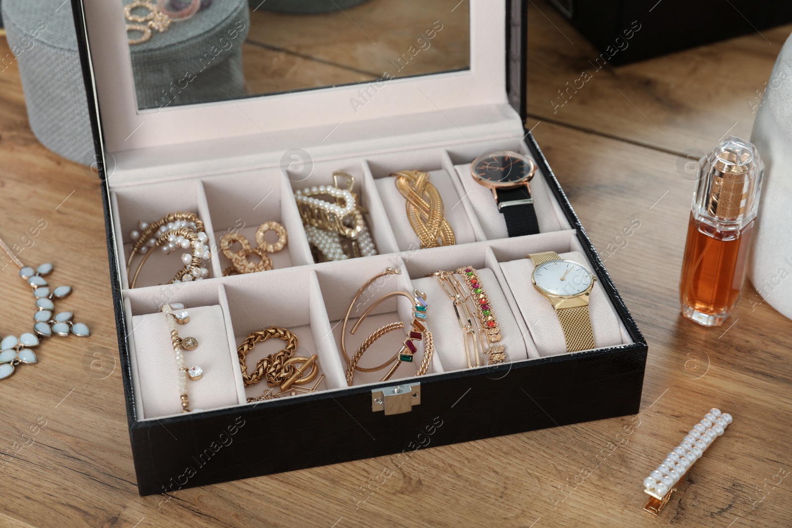 Photo of Elegant jewelry box with beautiful bijouterie and expensive wristwatches near luxury perfume on wooden table