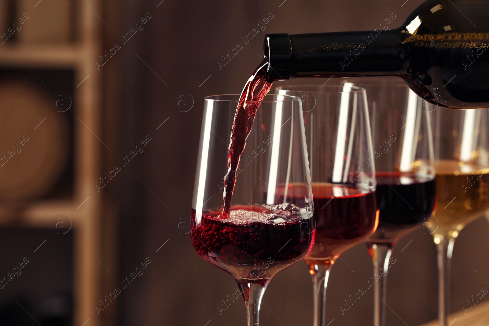 Photo of Pouring wine from bottle into glass in cellar, closeup