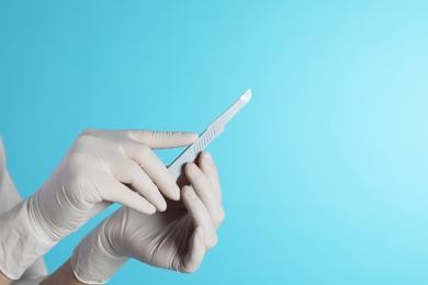 Photo of Female doctor holding scalpel on color background, closeup view with space for text. Medical object