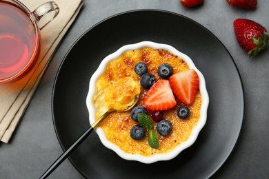 Photo of Delicious creme brulee with berries and mint in bowl served on grey table, flat lay