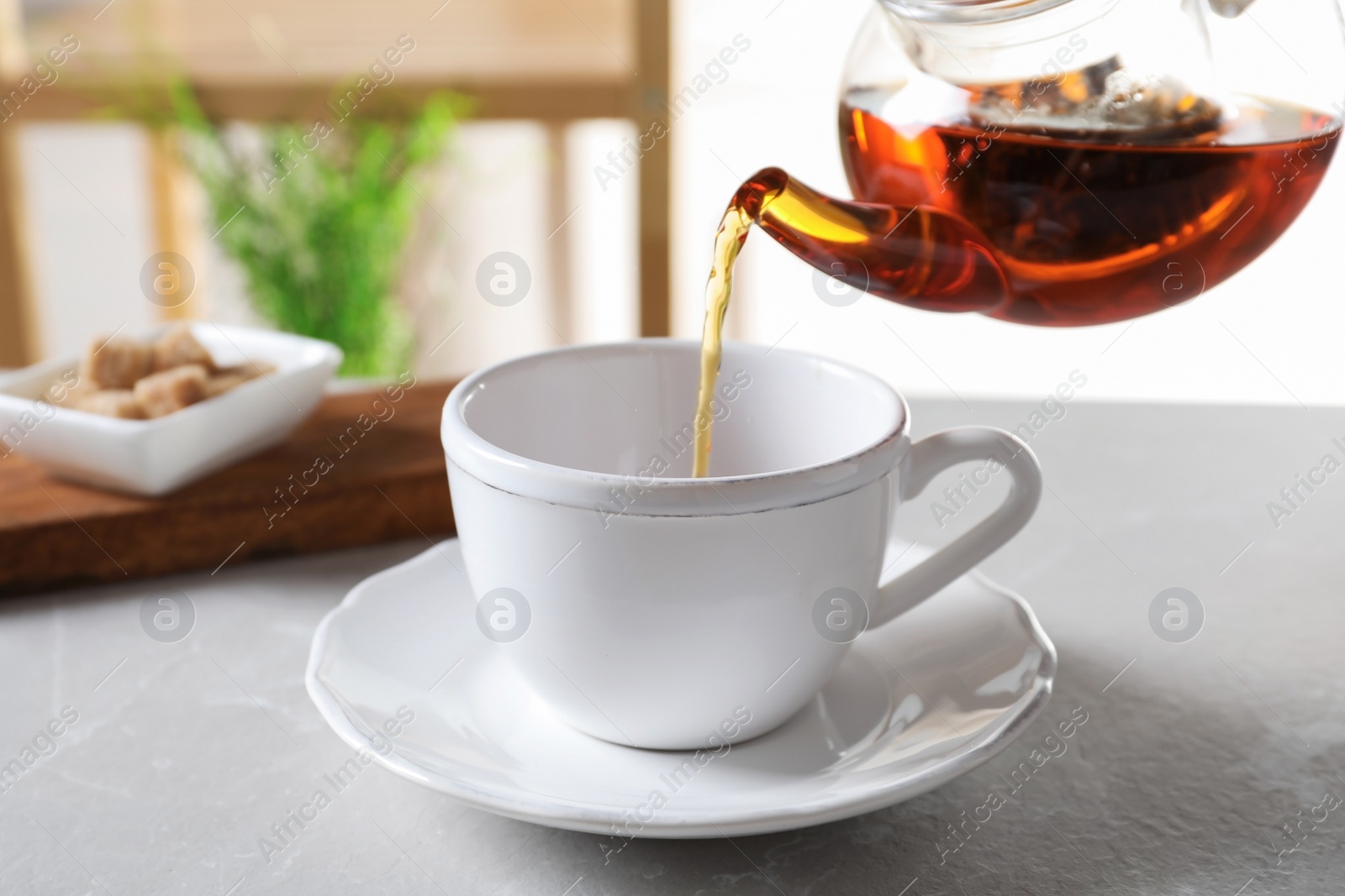 Photo of Pouring black tea into white porcelain cup on gray table