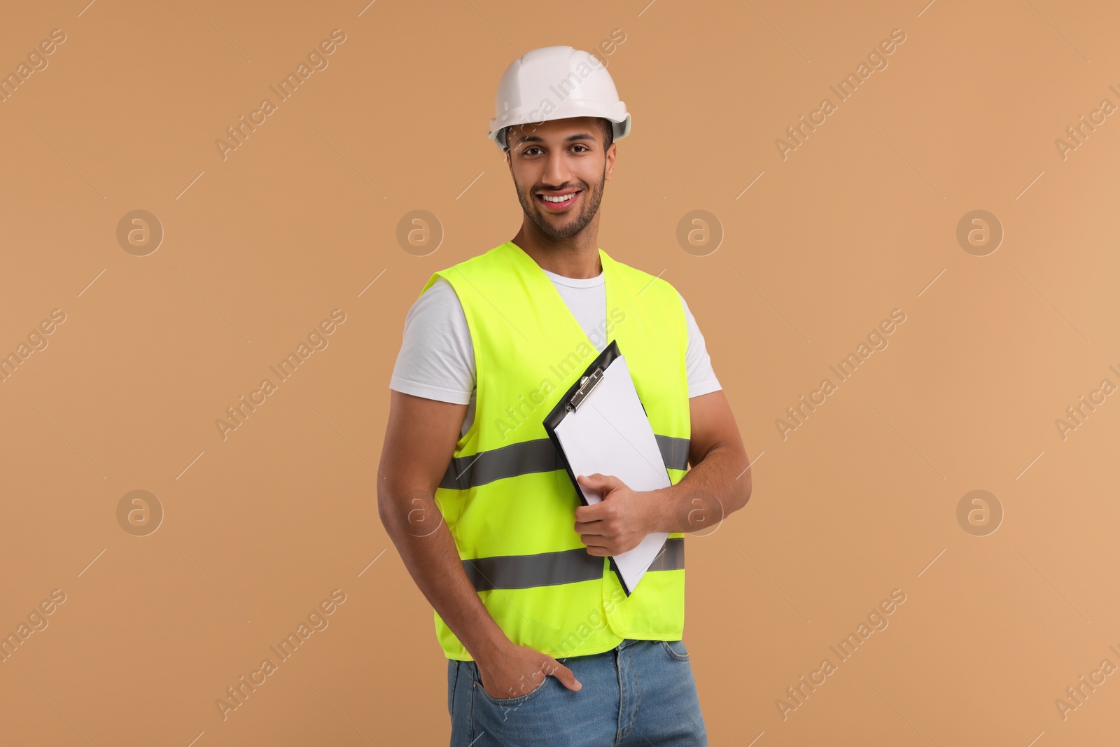 Photo of Engineer in hard hat holding clipboard on beige background