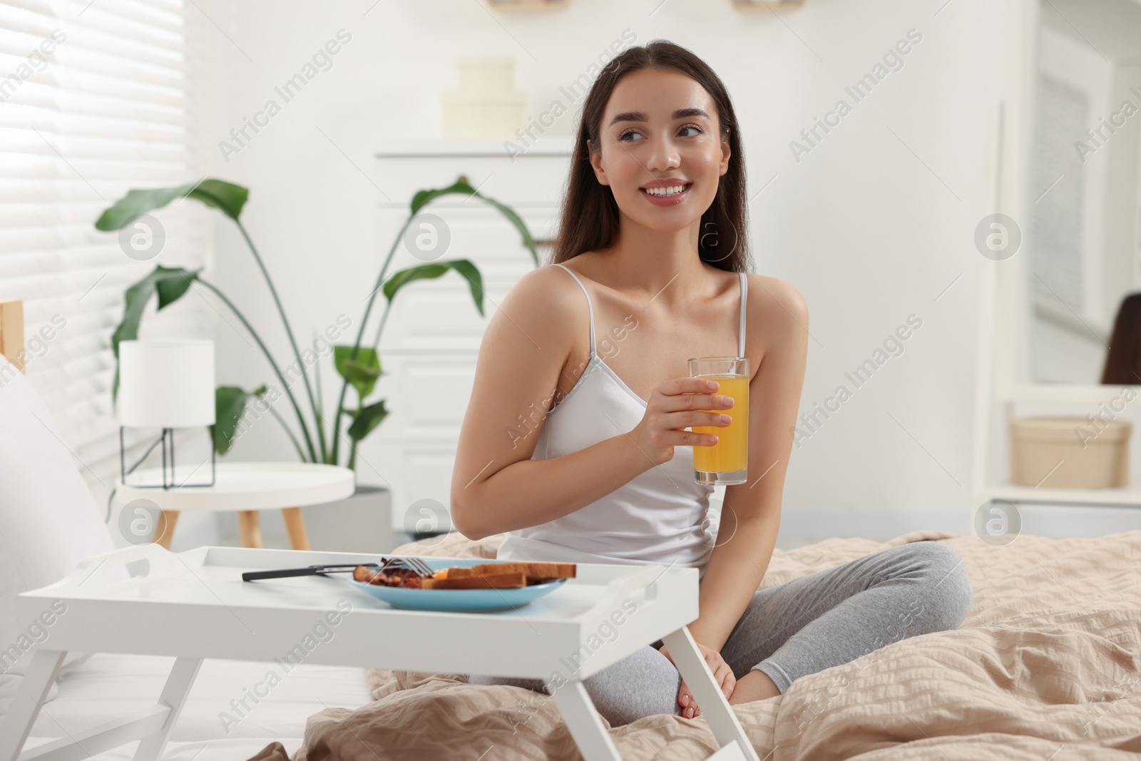 Photo of Happy young woman having breakfast on bed at home