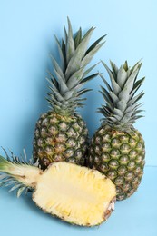 Photo of Whole and cut ripe pineapples on light blue background