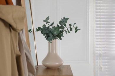 Photo of Beige ceramic vase with beautiful eucalyptus branches on table indoors