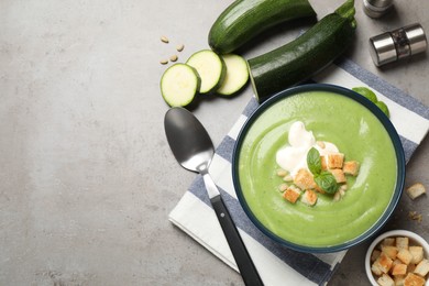 Tasty homemade zucchini cream soup on grey table, flat lay. Space for text