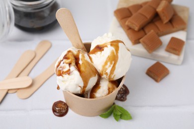 Scoops of ice cream with caramel sauce in paper cup on white tiled table