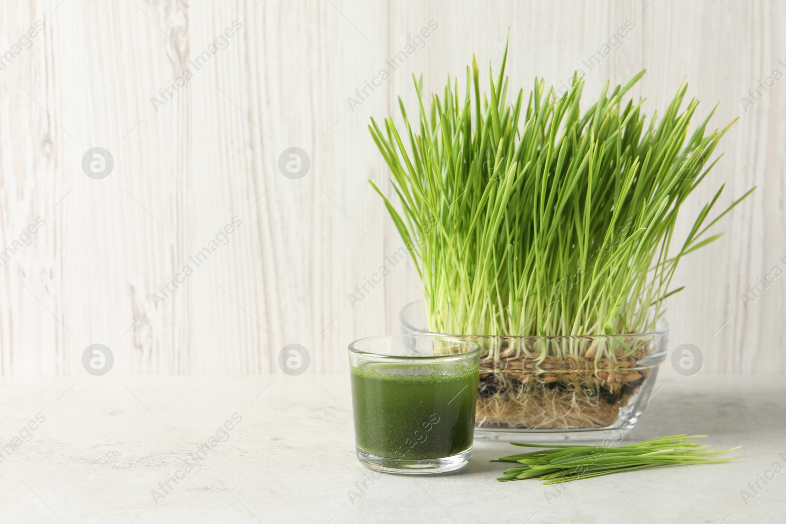 Photo of Wheat grass drink in glass and fresh sprouts on light table, space for text