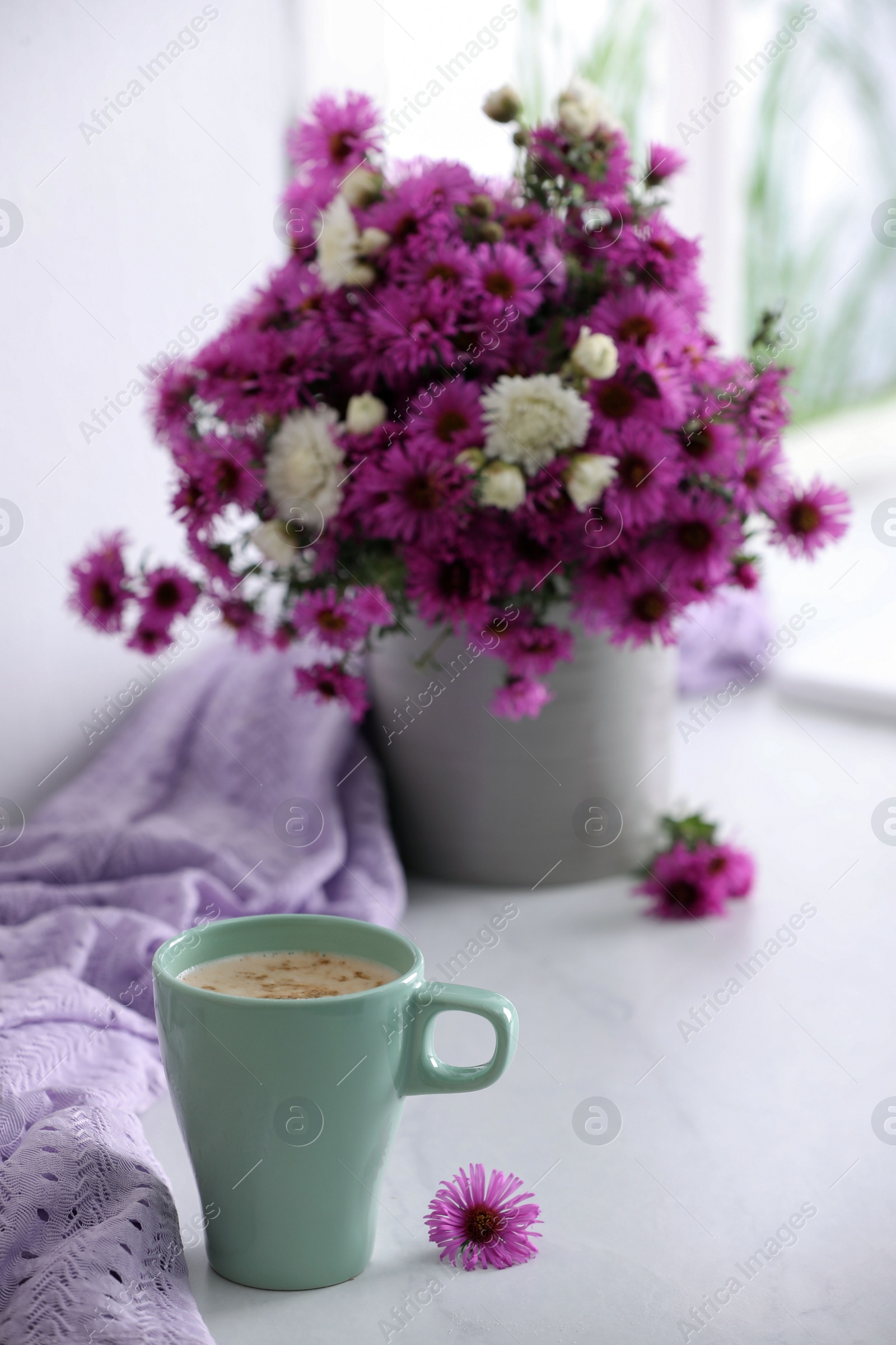 Photo of Cup of aromatic coffee, beautiful flowers and violet cloth on white table