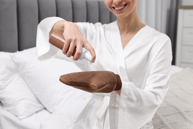 Photo of Self-tanning. Woman applying cosmetic product onto tanning mitt in bedroom, closeup
