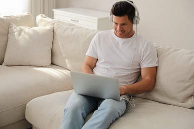 Photo of Man with laptop and headphones sitting on sofa at home