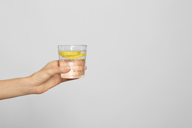 Photo of Young woman with glass of lemon water on light background, closeup. Space for text