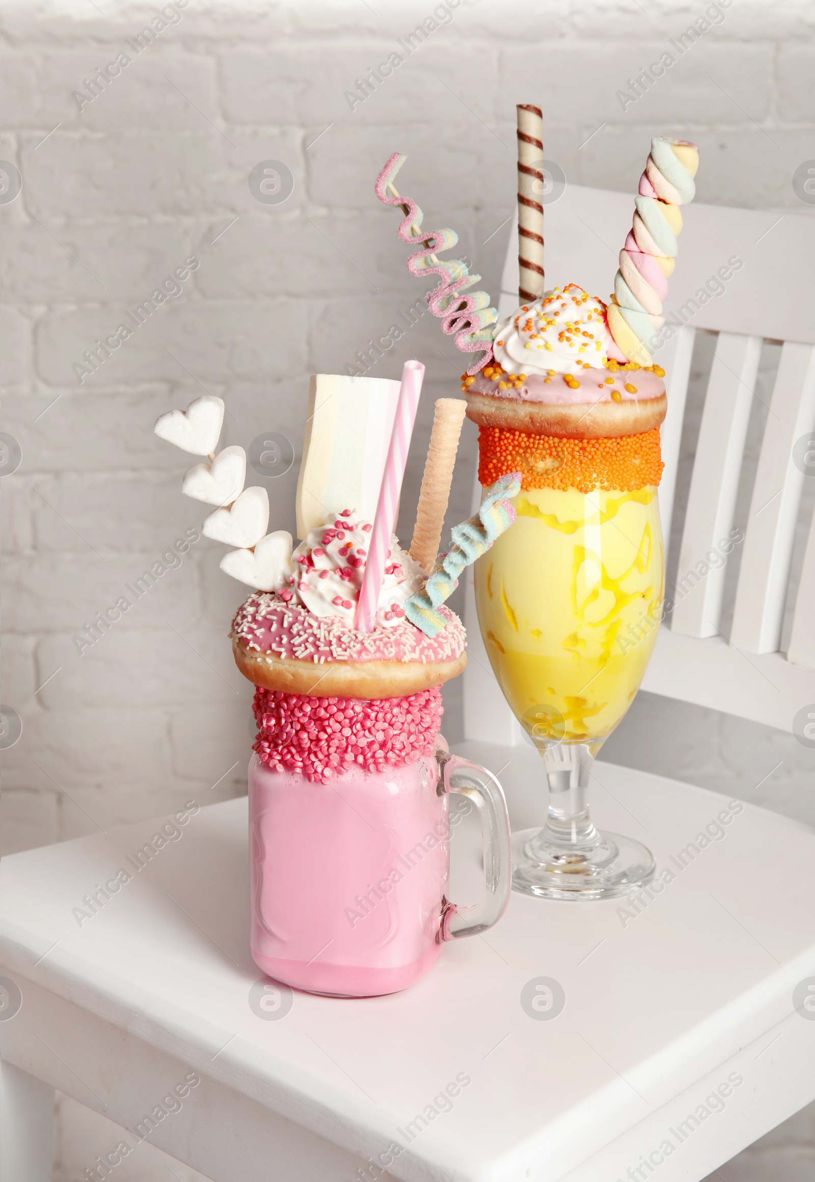 Photo of Tasty milk shakes with sweets in glassware on chair near brick wall